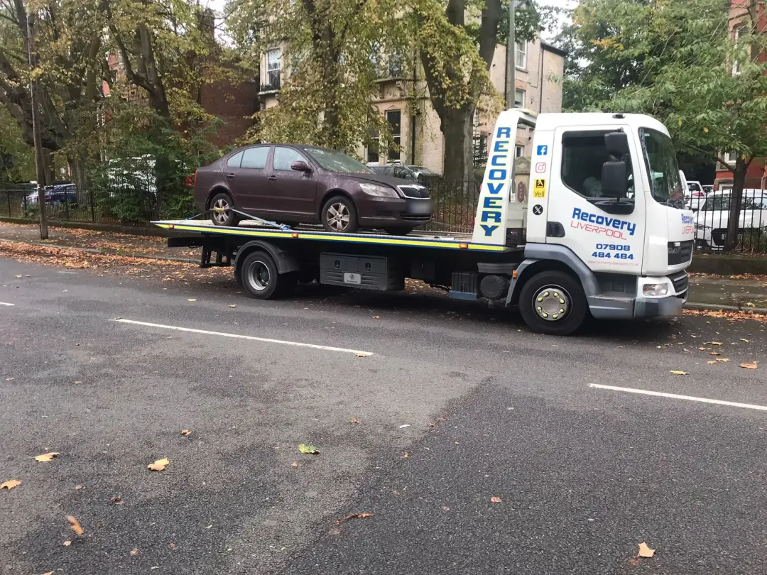 Saloon car strapped onto our recovery truck on a tree-lined street